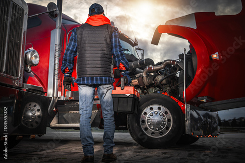 Foto Truck Driver Inspects Engine in Parking Lot During Sunset