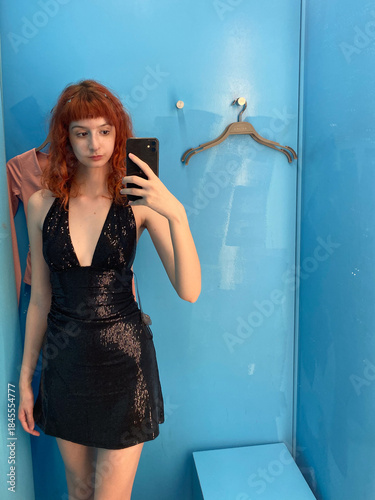 Young caucasian female trying black sequin dress in fitting room mirror selfie
