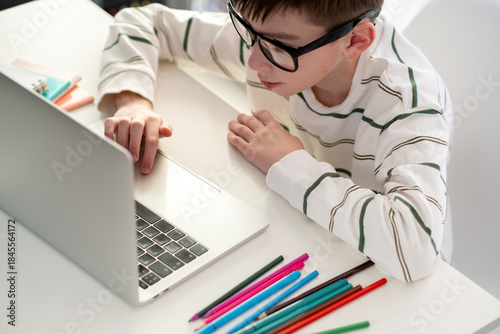 Slika na platnu cheerful Caucasian boy with headphones uses laptop to make video call with his teacher