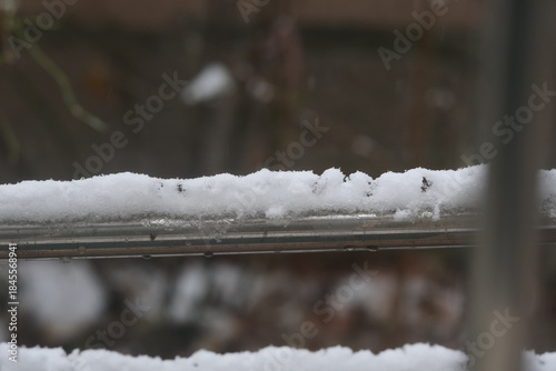 A close-up shot of thick, fresh snow resting on the metal railing of an outdoor structure during a snowy day.