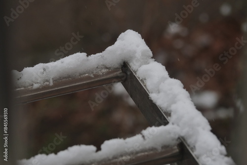 A close-up shot of thick, fresh snow resting on the metal railing of an outdoor structure during a snowy day.
