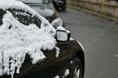A close-up shot of a car heavily covered in fresh, wet snow on a winter day.