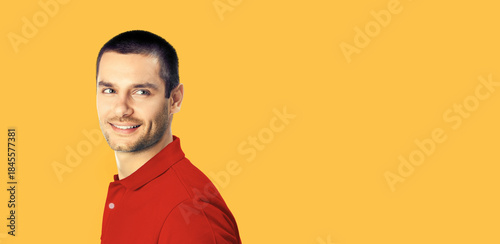 Portrait iof happy smiling young brunette hair man looking aside back, wear red t-shirt, isolated orange color background with free ad text space. Wide banner image
