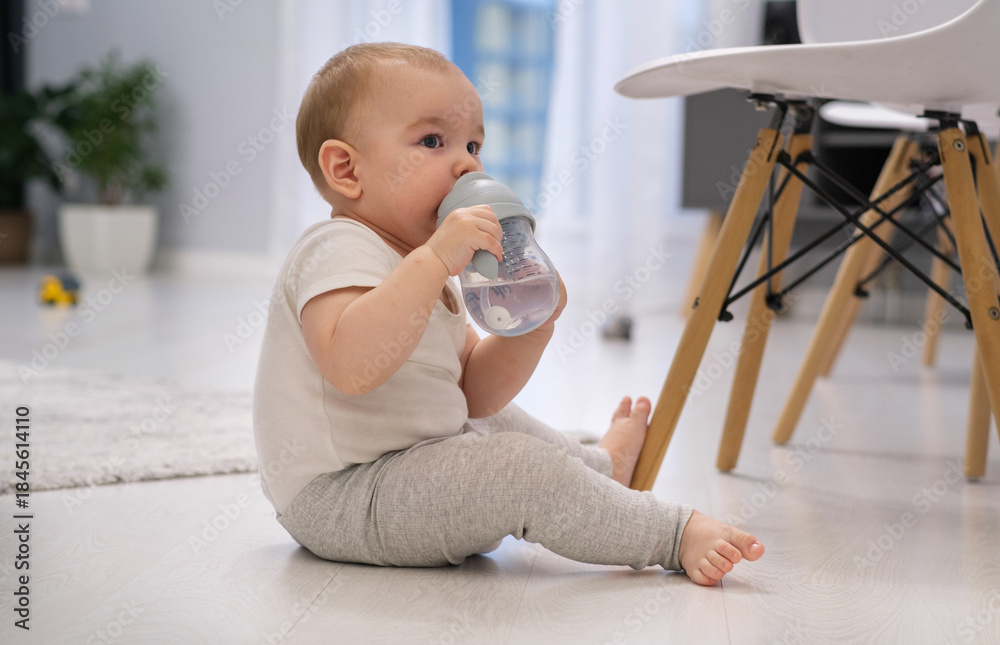 Obraz premium A baby is drinking from a bottle while sitting on the floor