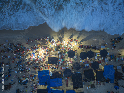 Aerial view of a bustling beach with vendors, marked by the rhythmic waves meeting the shore, casting long shadows across the sandy expanse, Tam Tien, Quang Nam, Vietnam