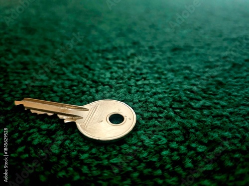 ​A silver metal door key lying on a textured dark green carpet. Close-up view with soft lighting and shallow depth of field. Useful for real estate.