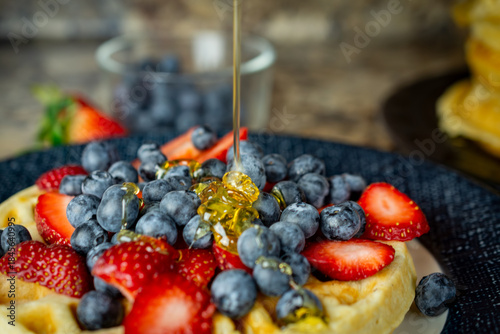 Golden honey is poured and drizzled over fresh blueberries and sliced strawberries on a waffle, completing the sweet breakfast in Waukesha County.