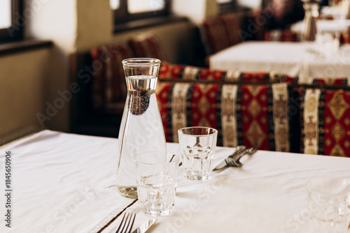 Glass carafe with water and glasses on empty restaurant table, copy space.