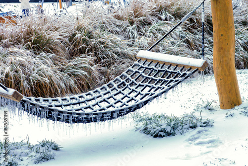 Frozen rope hammock with icicles hanging in winter snow covered garden