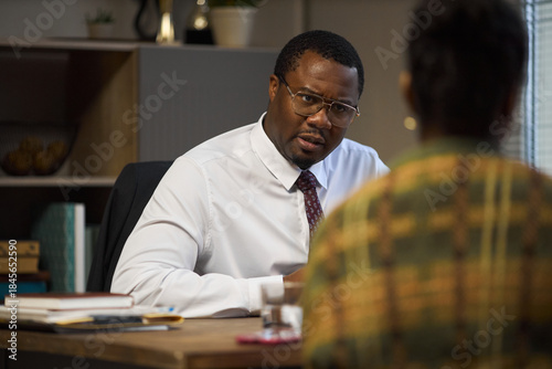 Valokuva Middle aged Black man wearing glasses sitting at desk talking to woman in office