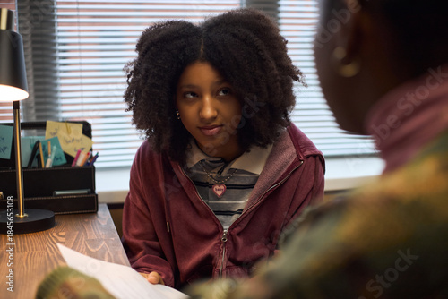 Foto Teenage Black girl sitting at desk listening attentively to middle aged Black wo