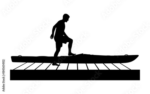 Silhouette of a man standing on a kayak on a dock.