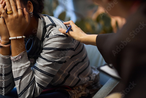 Canvas Print Black teenager sitting with head in hands being comforted by middle aged Caucasi