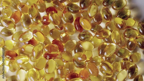 Top-down, close-up video of golden softgel capsules, like vitamin or fish oil supplements, slowly rotating on a turntable on white background showing concepts of healthcare, medicine, and nutrition.