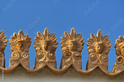 Fotografie Architectural detail in Athens, Greece showing a close-up of ornate roof decorations featuring stylized golden faces or masks with elaborate headdresses