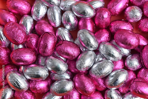 Pink and silver foil wrapped chocolate easter eggs, against a black background.