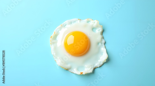 Minimalist pop art flat lay of a single, perfectly fried egg, sunny side up, on a solid pastel blue background.