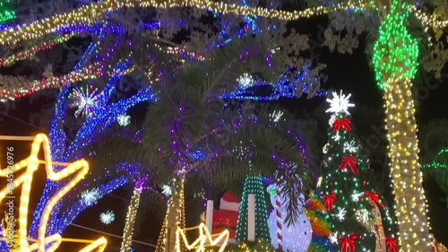 Bright reindeer light sculptures stand in a festive outdoor holiday display at night. Colorful LED lights, ornaments, and snowflake decorations create a magical winter atmosphere.