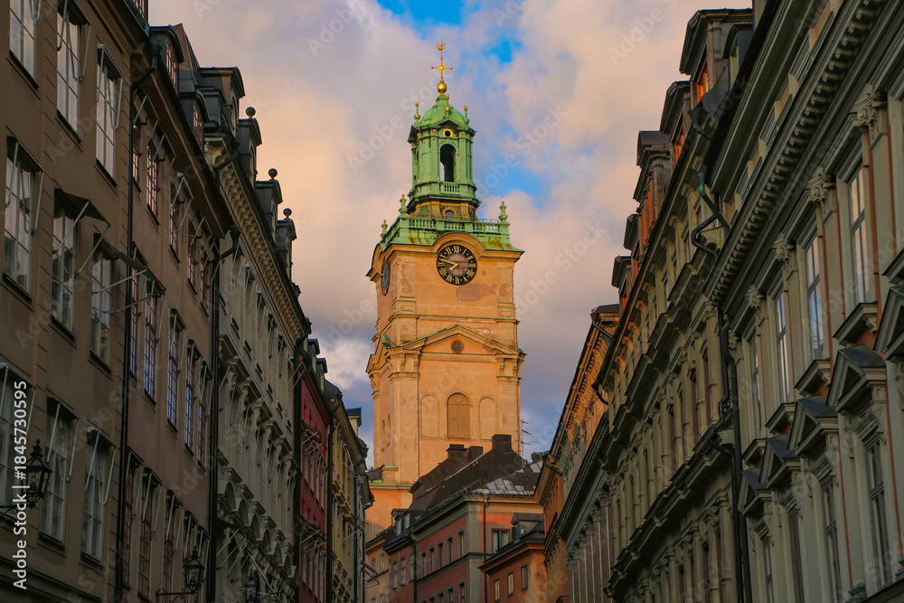 Fototapeta premium Clock tower of the Church of St Nicholas, behind a historic street of colourful buildings in the old town Gamla Stan, Stockholm, Sweden.