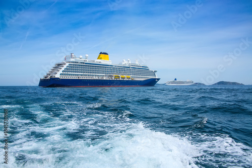 Cruise ship at anchor ourside St Peter Port, Guernsey. Large ship with blue hull and yellow funnel, and white ship in the distance, off the coast of the Channel Islands, UK.