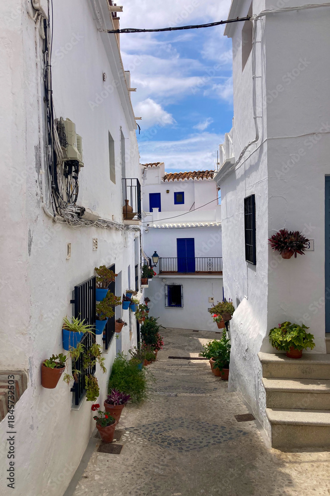 Fototapeta premium A peaceful walk through the charming narrow streets, surrounded by whitewashed houses and colorful flowers in Frigiliana, Spain