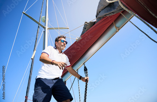 Fotografija sailboat skipper carefully collects the mainsail, preparing the vessel to safely enter port after a sailing journey