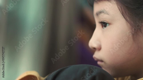 Close up side profile of sad Asian girl face looking away with selective focus. Lonely child sitting near window feeling bored, depressed, unhappy, thinking or waiting in solitude at home.