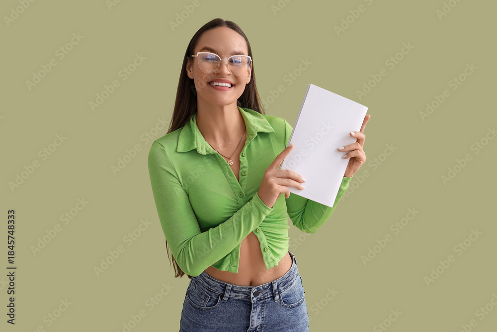 Fototapeta premium Young woman with blank magazine on green background