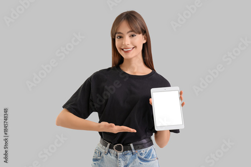 Young woman with blank tablet computer on light background