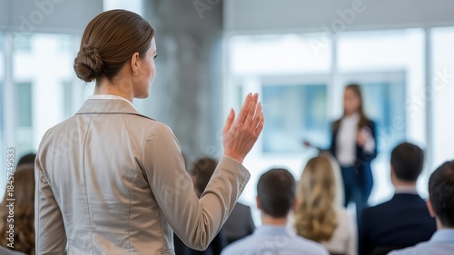 A woman in a suit raises her hand to ask a question during a business presentation.