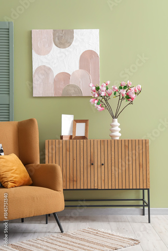 Interior of living room with commode, armchair and magnolia flowers in vase