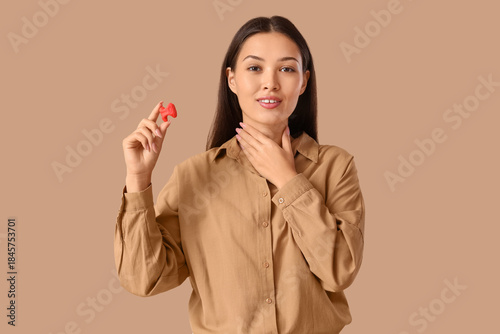 Young Asian woman with thyroid gland model on beige background