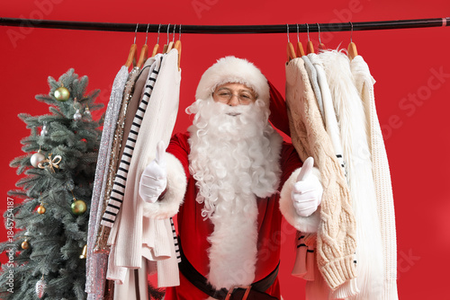 Santa Claus and rack with different clothes near Christmas tree on red backgr...