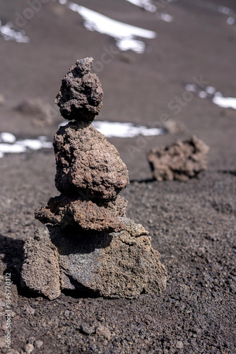 Stacked volcanic stones forming a small cairn on the slopes of Mount Etna, Sicily. Minimalistic rock formation symbolizes balance, human presence, and harmony within harsh volcanic landscape shaped