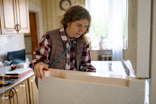 Woman standing in a home kitchen looking into an open refrigerator, checking food and ingredients for a meal