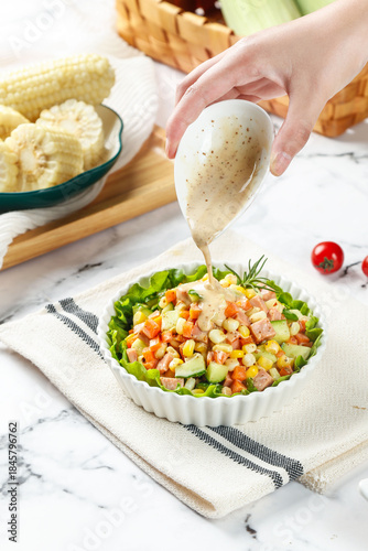 Pouring Dressing Over Fresh Vegetable Salad with Corn and Ham