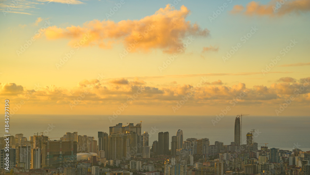 Fototapeta premium Panoramic view of a city along the coastline during a vibrant sunset, highlighting urban architecture, water reflections, and warm evening light. Perfect for travel, cityscape, or coastal projects.