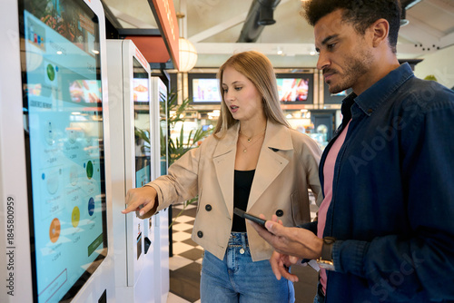 Couple using self service kiosk to order food in restaurant