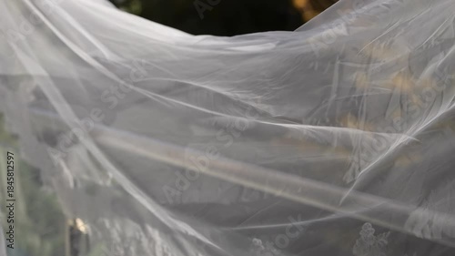 Flowing Wedding Veil Outdoors In Breeze, Translucent Tulle Drifts Across Sunlit Garden, Soft Highlights And Gentle Folds Create Romantic