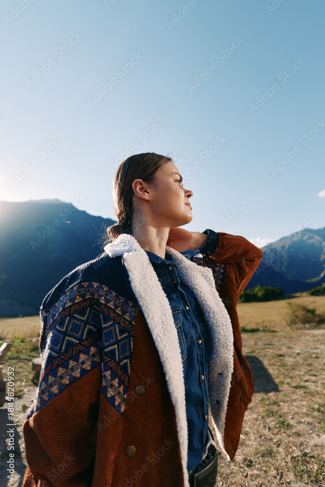 Fototapeta premium Woman in mountains wearing a warm jacket outdoors, portrait in nature with sunlight on face and meadow background, young traveler with braided hair enjoying scenic landscape.