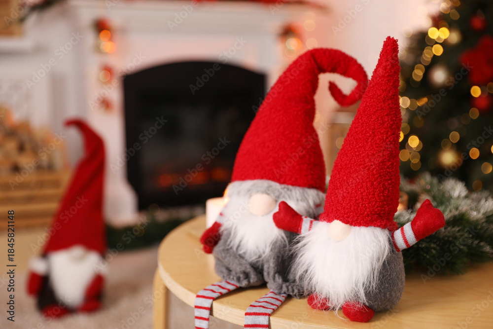 Fototapeta premium Cute Christmas gnomes on wooden table against blurred lights indoors, closeup. Space for text