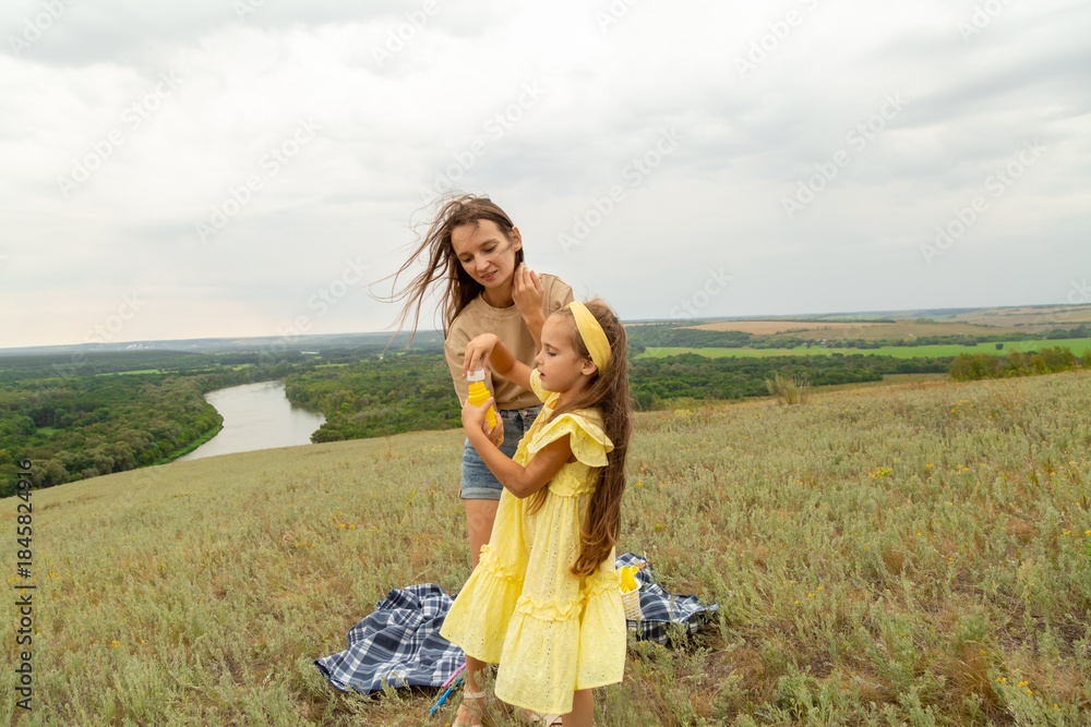 Obraz premium Mother with daughter blowing soap bubbles in field on summer day