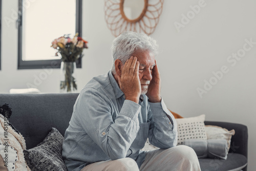 Foto Mature man sits on a sofa holding his head in discomfort