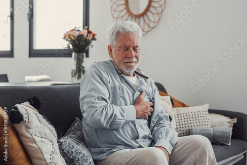 Fotografía Old man sits on a sofa clutching his chest in distress