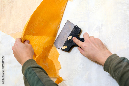 A man is tearing off old wallpaper from a wall.
