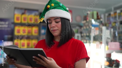 Happy female employee wearing a christmas elf hat writing in a notebook and giving a thumbs up