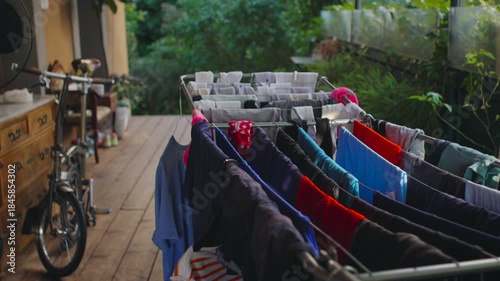 Wallpaper Mural Laundry drying rack filled with colorful garments on balcony near bicycle and dresser, domestic chore moment expressing everyday rhythm inside warm lived family home Torontodigital.ca