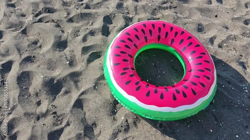 Vibrant pink and green swim ring adorned with a fun watermelon pattern rolling along the sandy beach. Capturing the essence of a dreamy summer getaway
