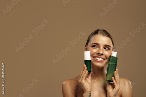 Young woman with glowing skin holding two green skincare bottles