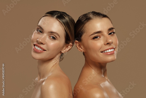 Beautiful women with radiant skin posing back to back on beige background